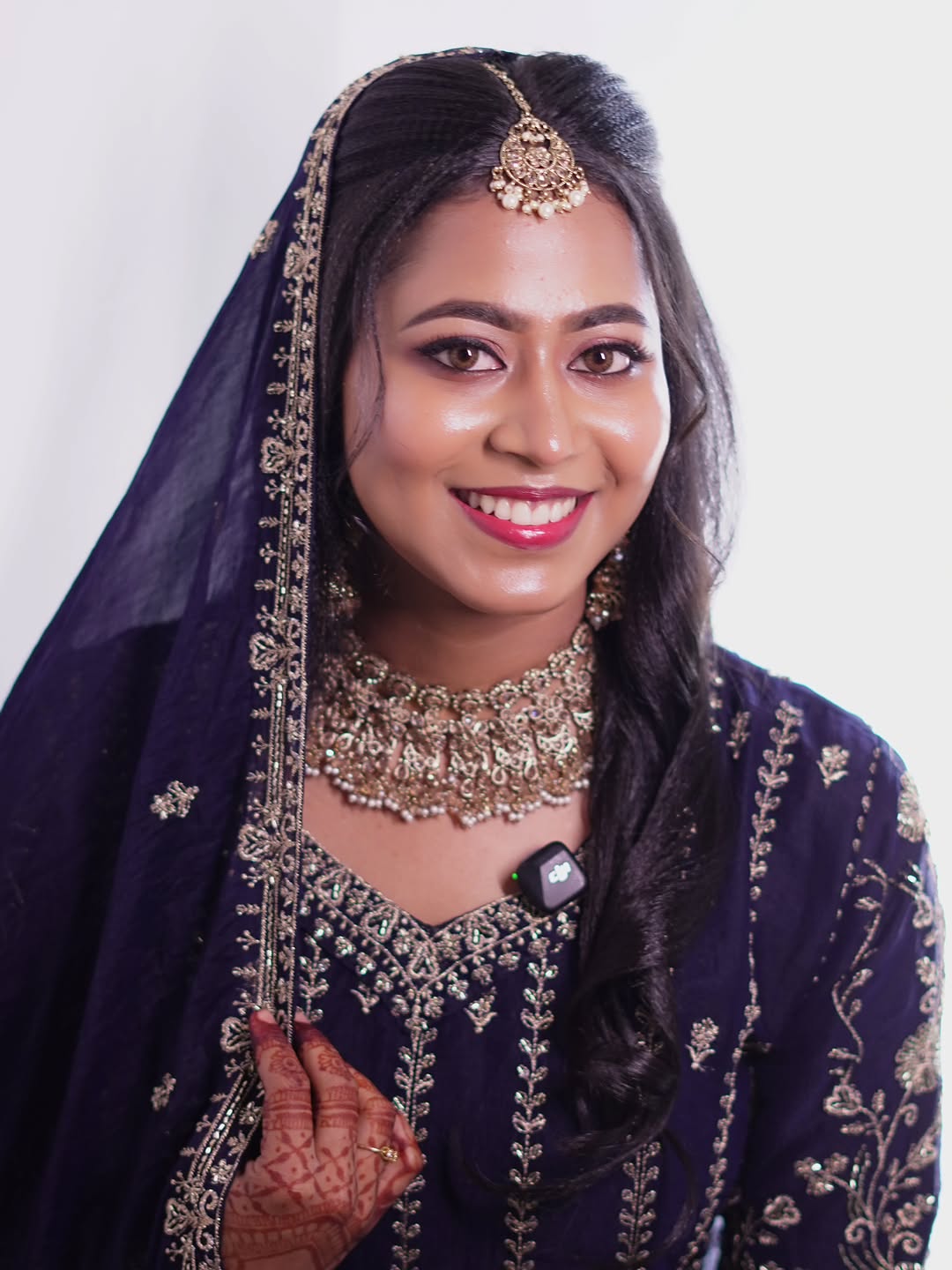 A bride in navy and gold with a gold choker and mehendi