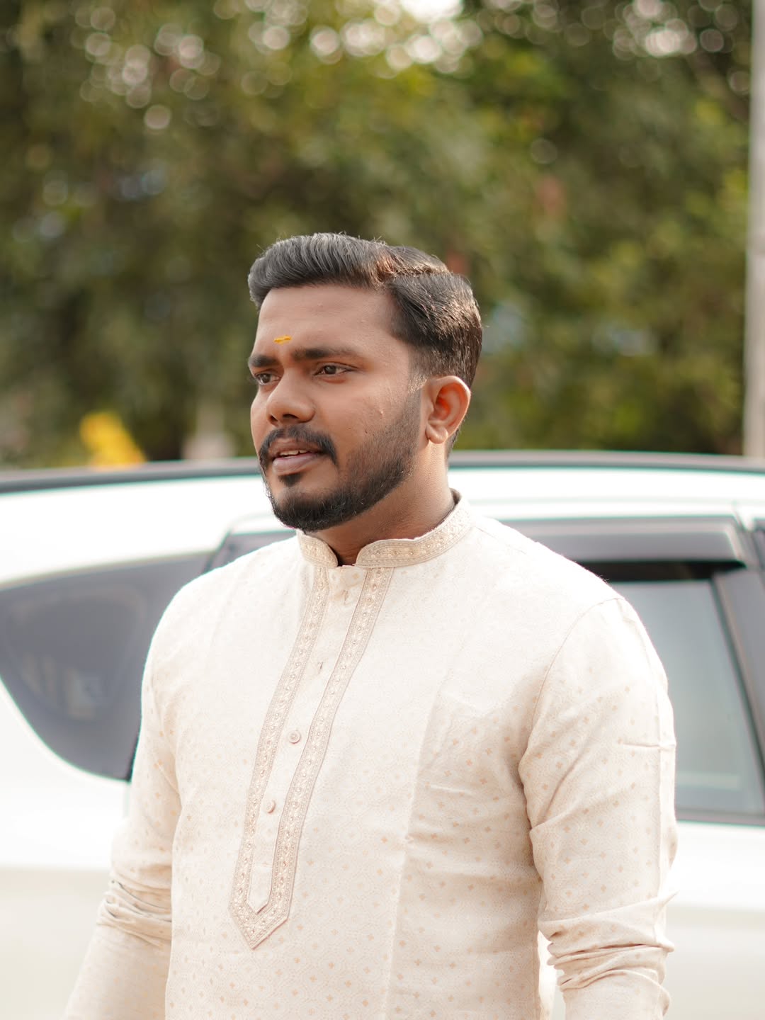 A groom in a cream kurta with a sharp cut and trimmed beard